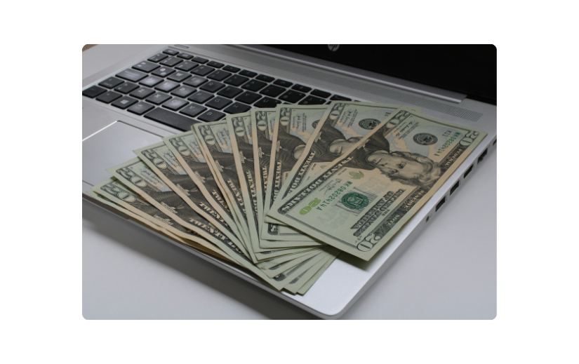 Stack of U.S. dollar bills spread out on a laptop, representing AI for online sales and digital business profitability.